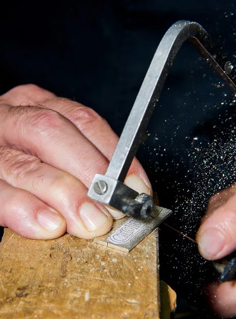 Manos de un artesano de TOUS trabajando una pieza con una sierra de joyero